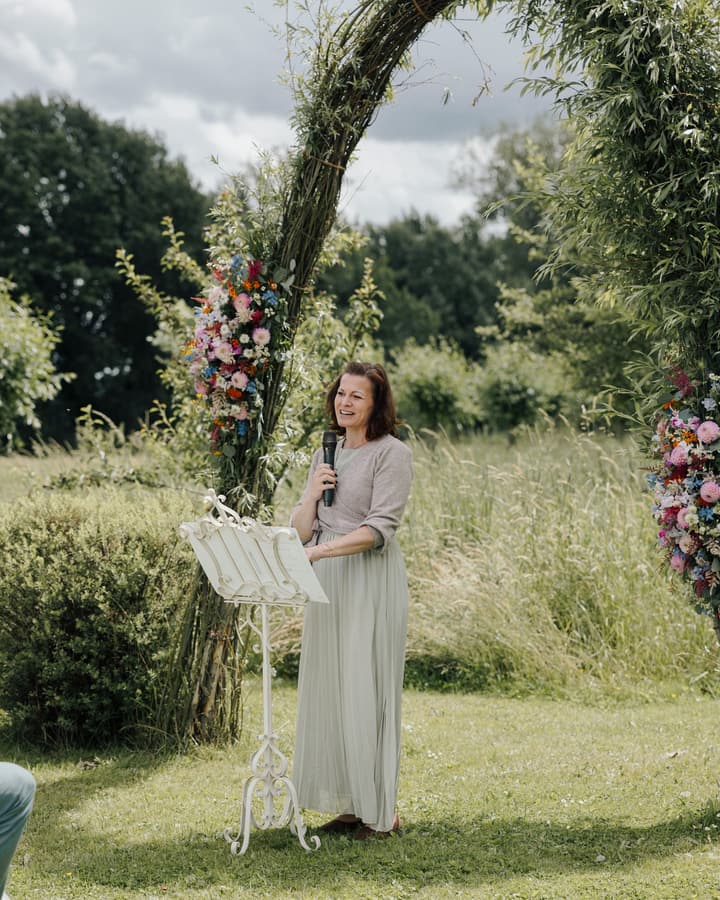 Jasmina van Thiel spricht an ihrem Notenpult unter einem Blumenbogen auf einer Wiese