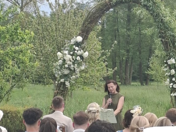 Jasmina van Thiel spricht vor den Gästen unter einem Blütenbogen auf der Wiese
